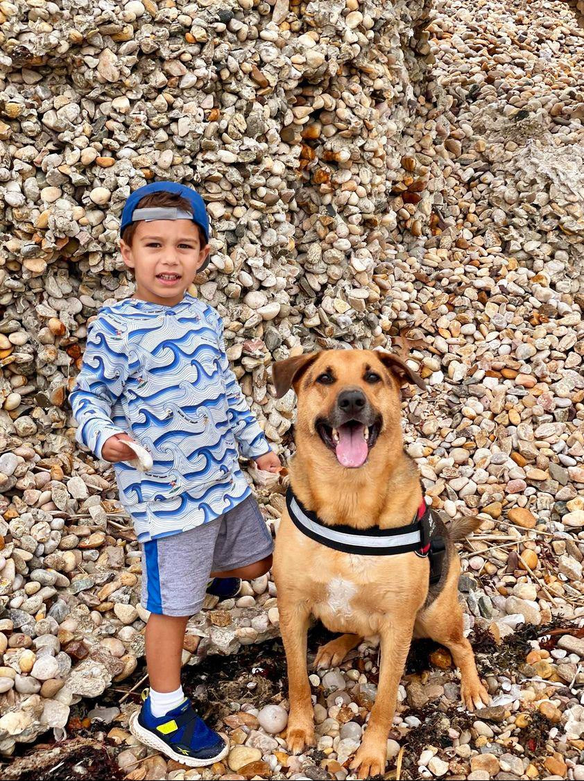 Toddler at rocky beach happily posing with his dog while wearing the organic surf hoodie