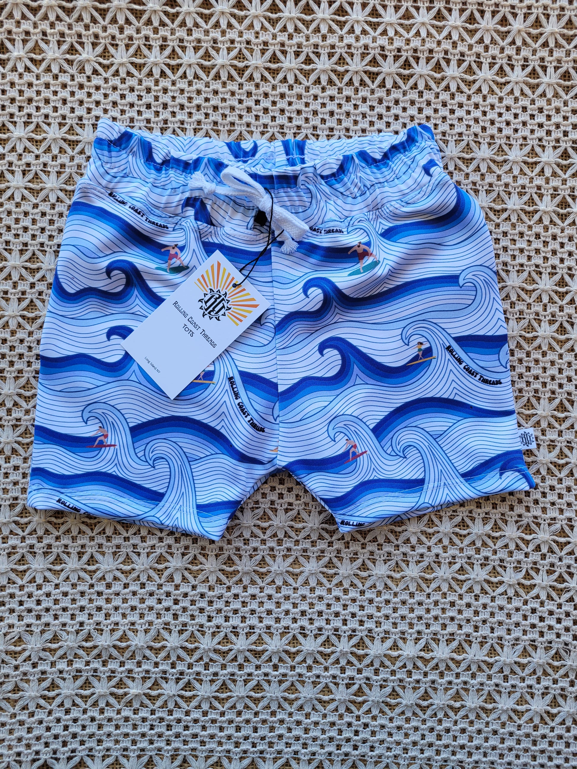 Front of Boys swim shorts. White and blue waves with surfers