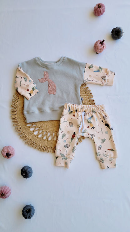 Flat lay of baby outfit set with seafoam green mermaid patch crewneck and pink joggers featuring ocean-themed print, surrounded by decorative fabric pumpkins.
